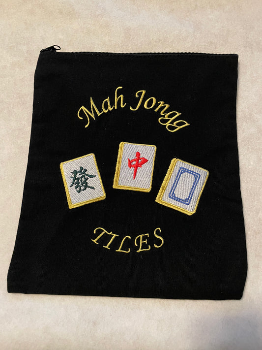 Black mahjong-themed zippered accessory pouch featuring gold embroidered "Mah Jongg Tiles" lettering and three decorative mahjong tiles in green, red, and blue with gold borders.