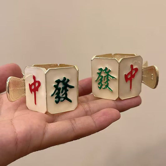 Pair of gold-tone mahjong-themed cufflinks featuring ivory-colored tiles with raised red and green Chinese characters representing the Red Dragon and Green Dragon mahjong tiles, displayed in a hand.
