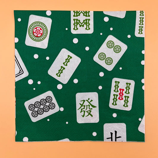 Green mahjong-themed napkin featuring a scattered pattern of traditional mahjong tiles with bamboo, dot, and Chinese character designs in green, red, and black, accented with white polka dots.