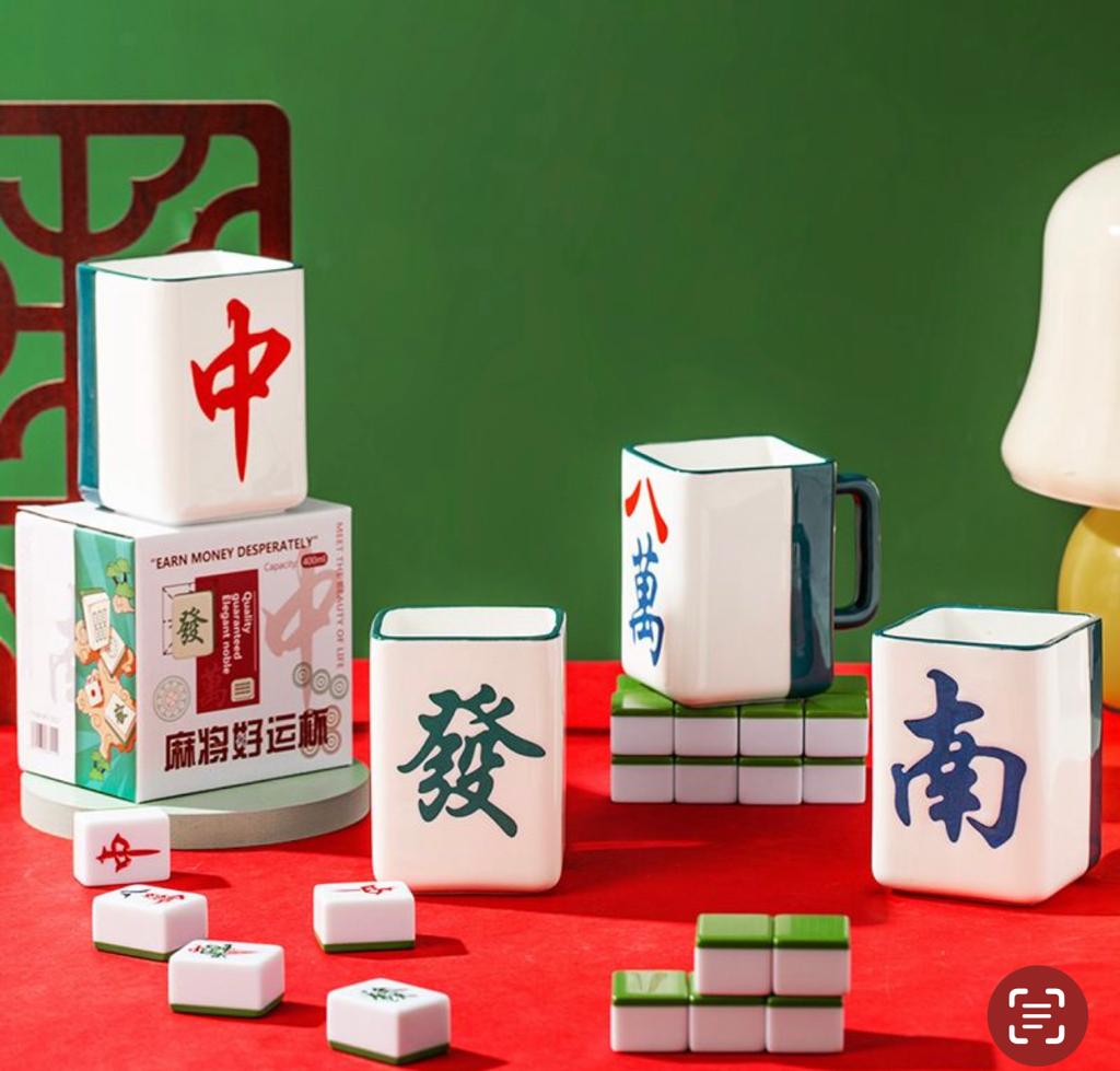 Set of four mahjong-themed ceramic mugs featuring traditional Chinese characters representing Red Dragon, Green Dragon, South Wind, and Eight of Characters tiles, displayed on a red table with green mahjong tiles.