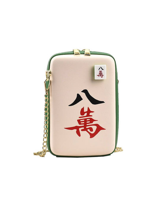 Mahjong-inspired crossbody bag featuring a beige exterior, green trim, gold chain strap, and bold red and black Chinese characters representing the Eight of Characters mahjong tile.