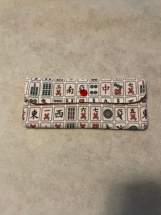 Mahjong-themed fabric accessory pouch featuring a colorful pattern of traditional mahjong tiles in red, green, and black on a beige background, with a fold-over flap and red button closure.