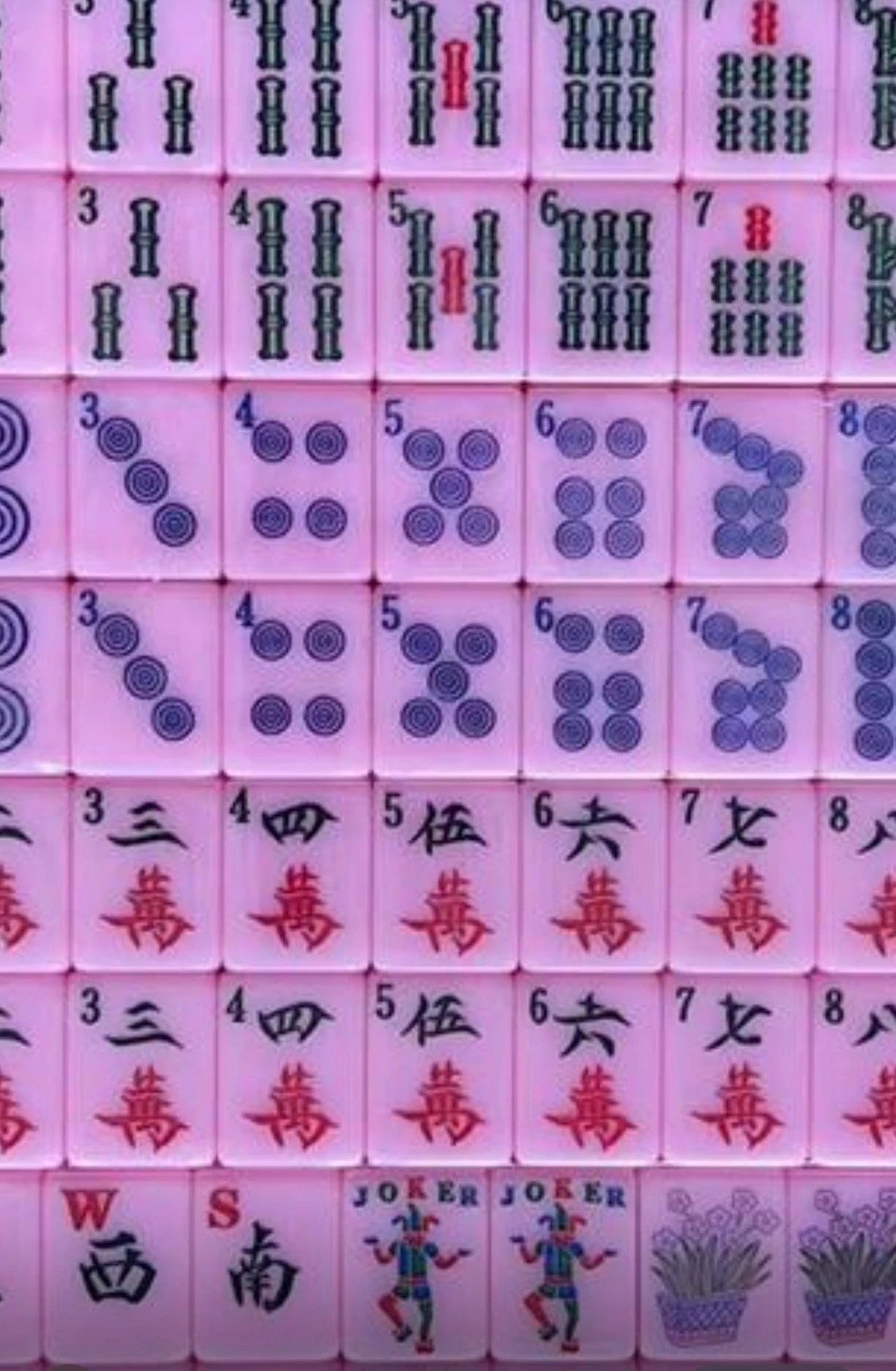 Close-up of a pink mahjong tile set featuring traditional bamboo, dots, Chinese character, wind, flower, and joker tiles arranged in rows with colorful designs.