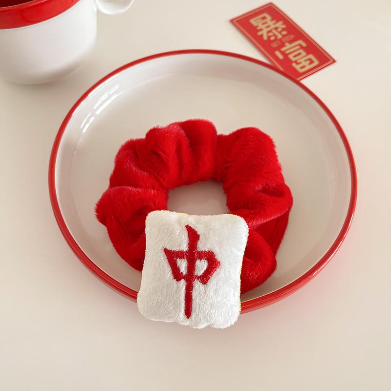Red plush mahjong-themed hair scrunchie featuring a soft white mahjong tile decoration embroidered with the red Chinese character representing the Red Dragon tile, displayed on a white plate.